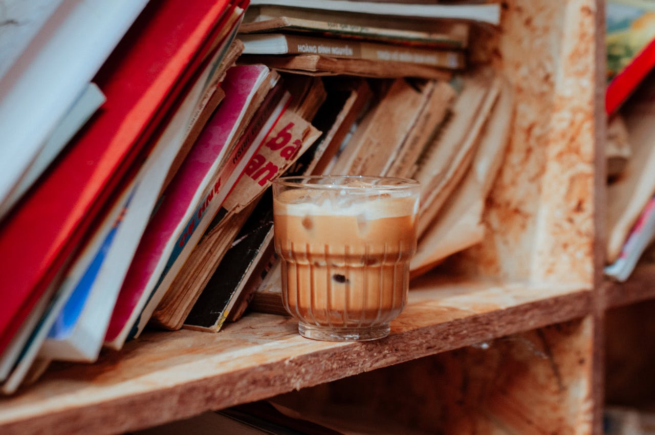 A creamy iced coffee placed on a rustic wooden shelf surrounded by books.