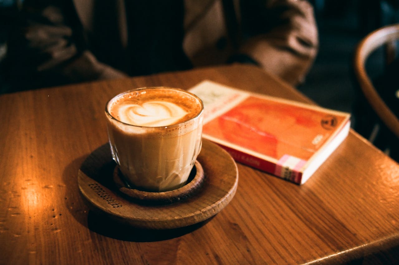 A cozy cappuccino with latte art beside a book on a wooden table in a cafe setting.