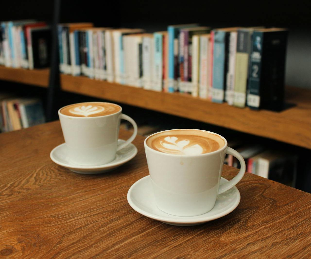 Two cups of cappuccino with latte art on a wooden table in a library.