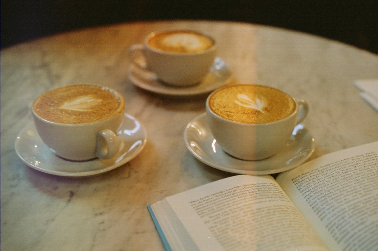 Three cups of latte on a marble table beside an open book in an Istanbul cafe, offering a warm coffee moment.